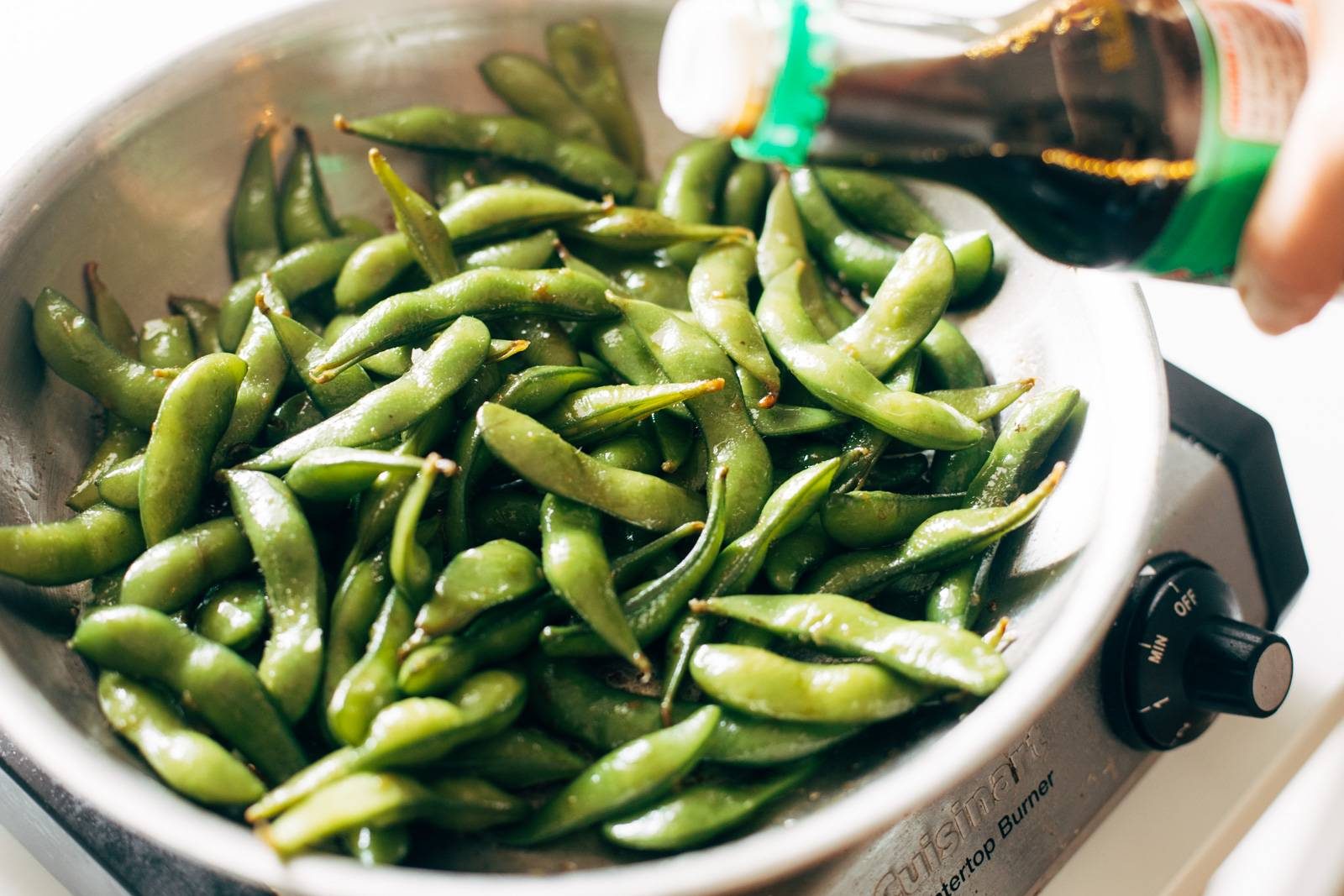 Pouring soy sauce into a pan of garlic edamame.