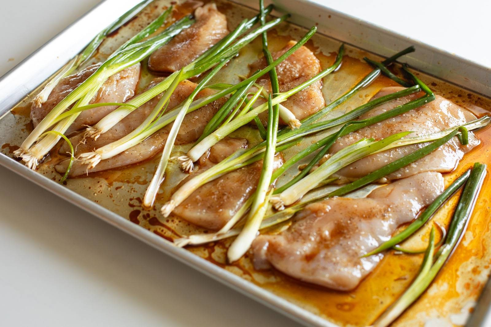 Scallions arranged over chicken on a sheet pan.
