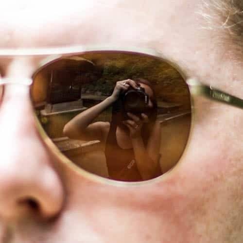 Woman taking a photo of herself in a man's sunglasses.