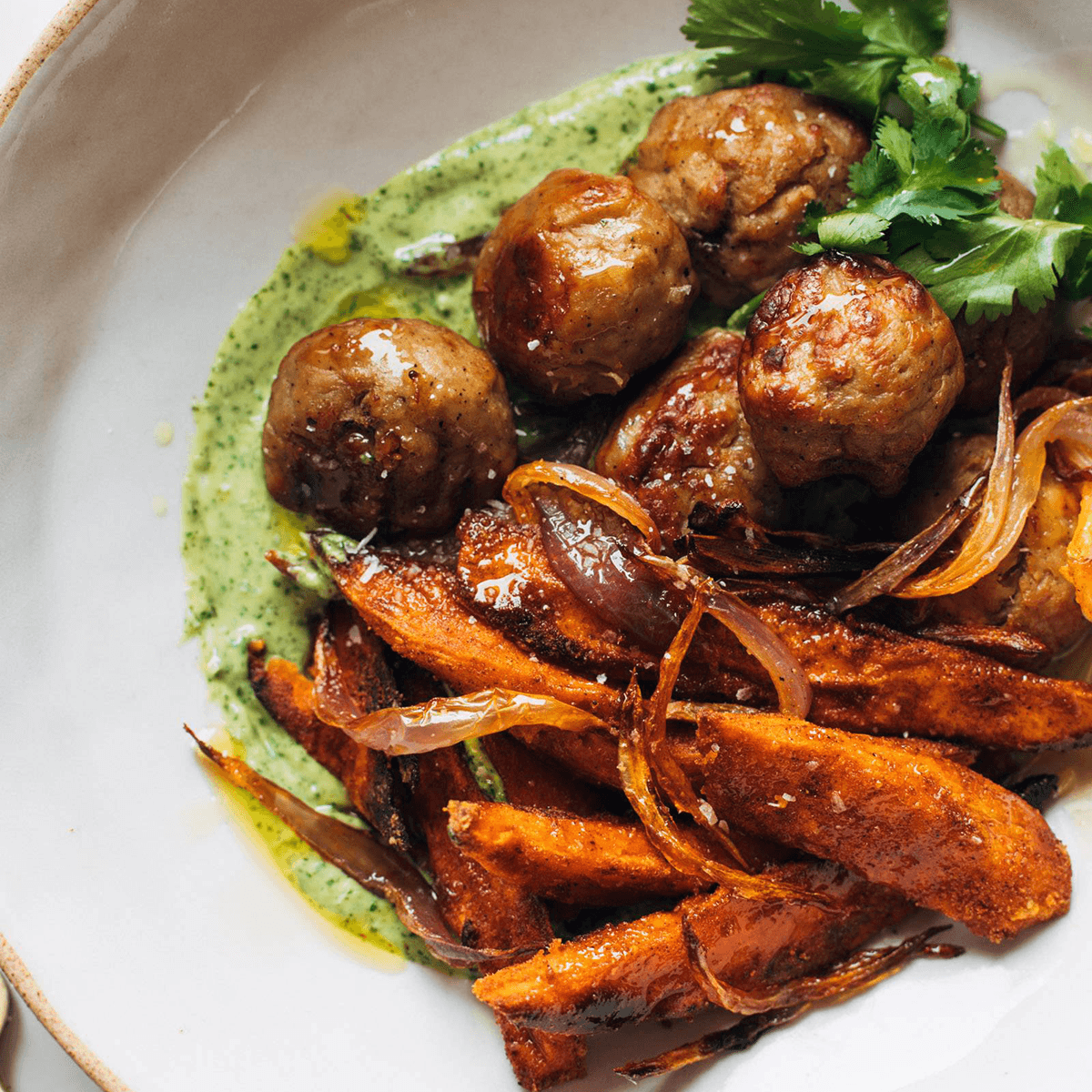 Meatballs in a bowl with sweet potatoes and aji verde.