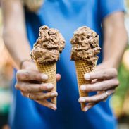 Person holding two chocolate ice cream cones.