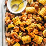 Shrimp, potato and corn mixture on a sheet pan with a side of melted butter in a bowl.