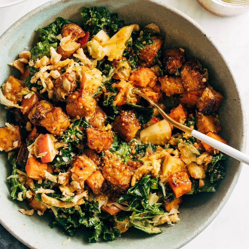 Crispy tempeh with green leafy vegetables in a bowl with a spoon.