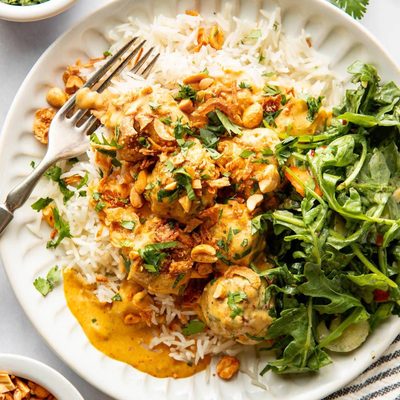 Yellow curry meatballs on a plate with rice and greens.