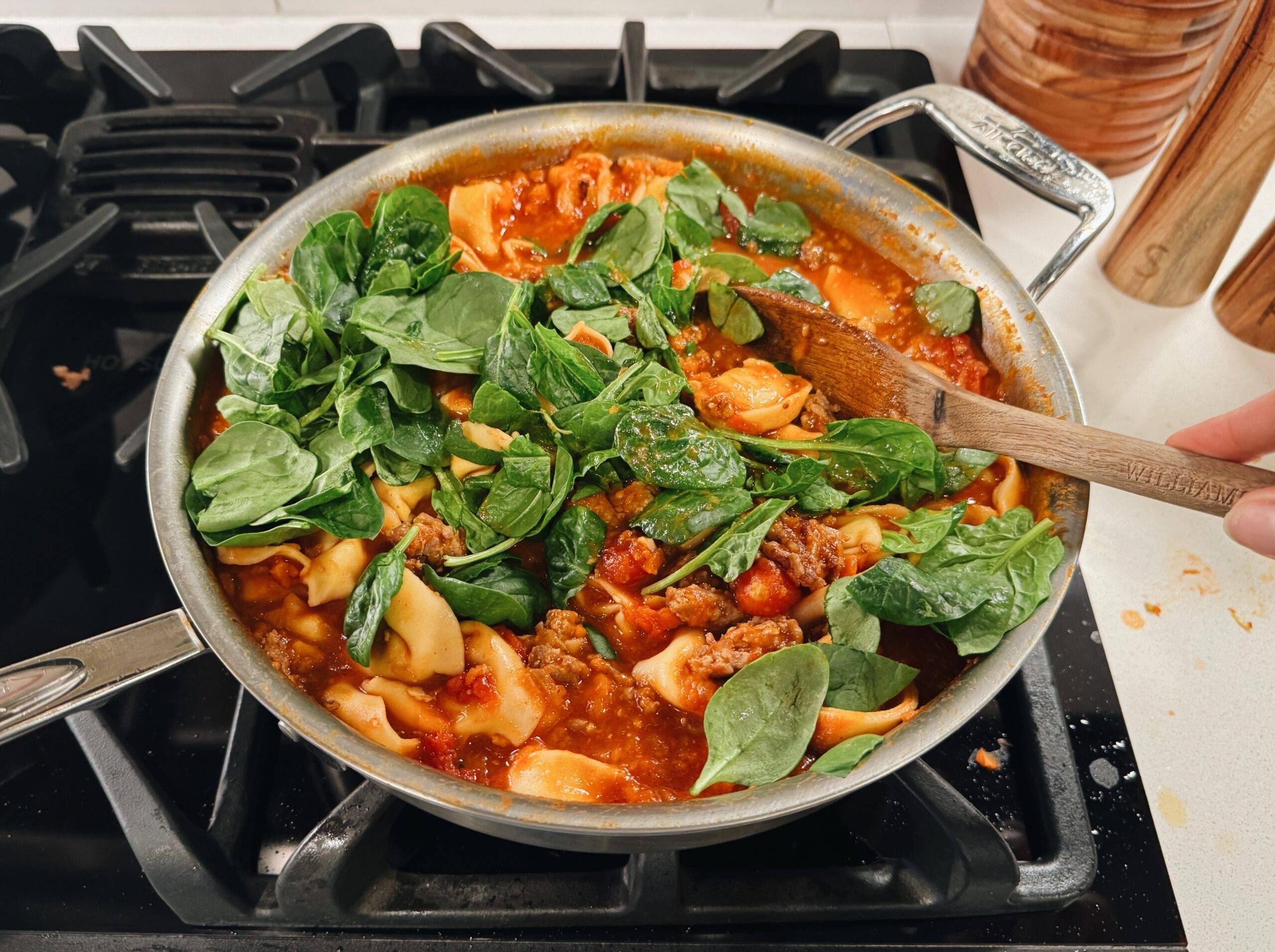 Adding spinach to pan of tortellini.