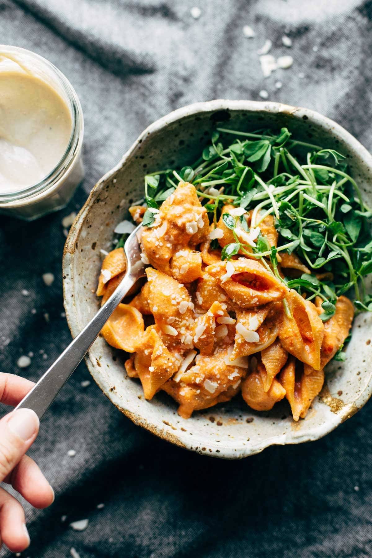 Creamy tomato shells and greens in a bowl with a fork.