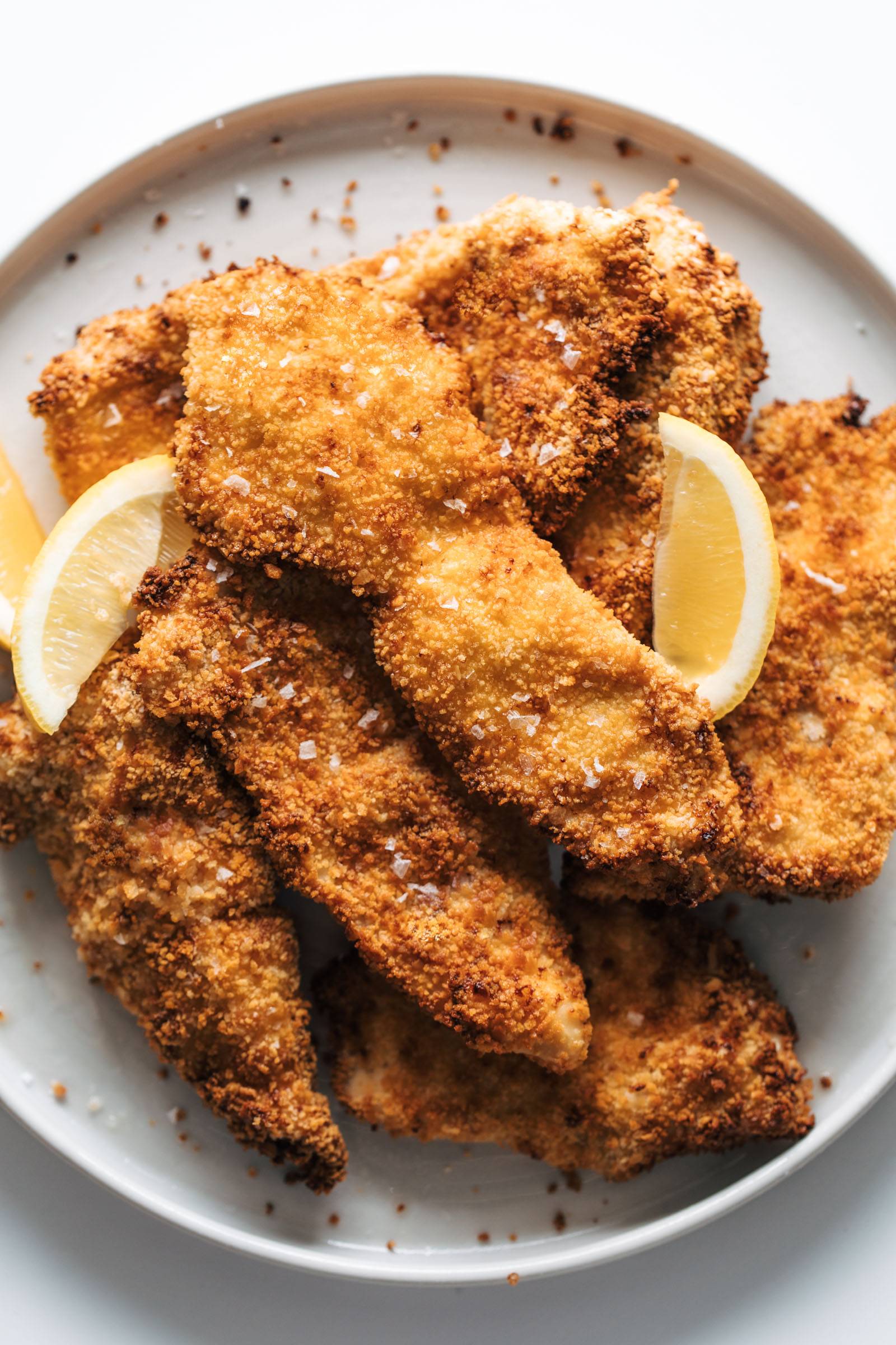 Crispy chicken cutlets on a plate with lemon slices.