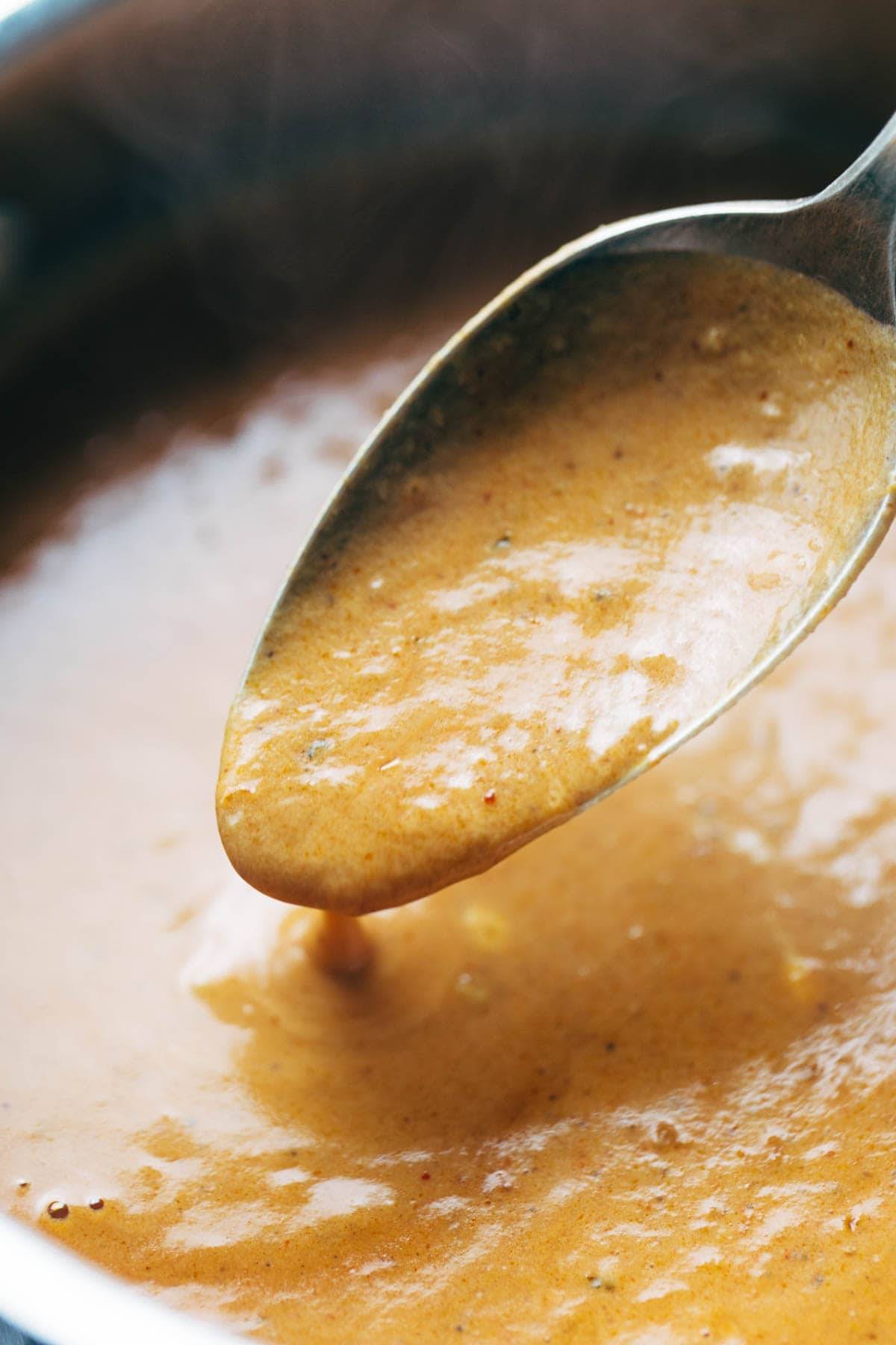 Masala sauce simmering in a pan with a spoon.