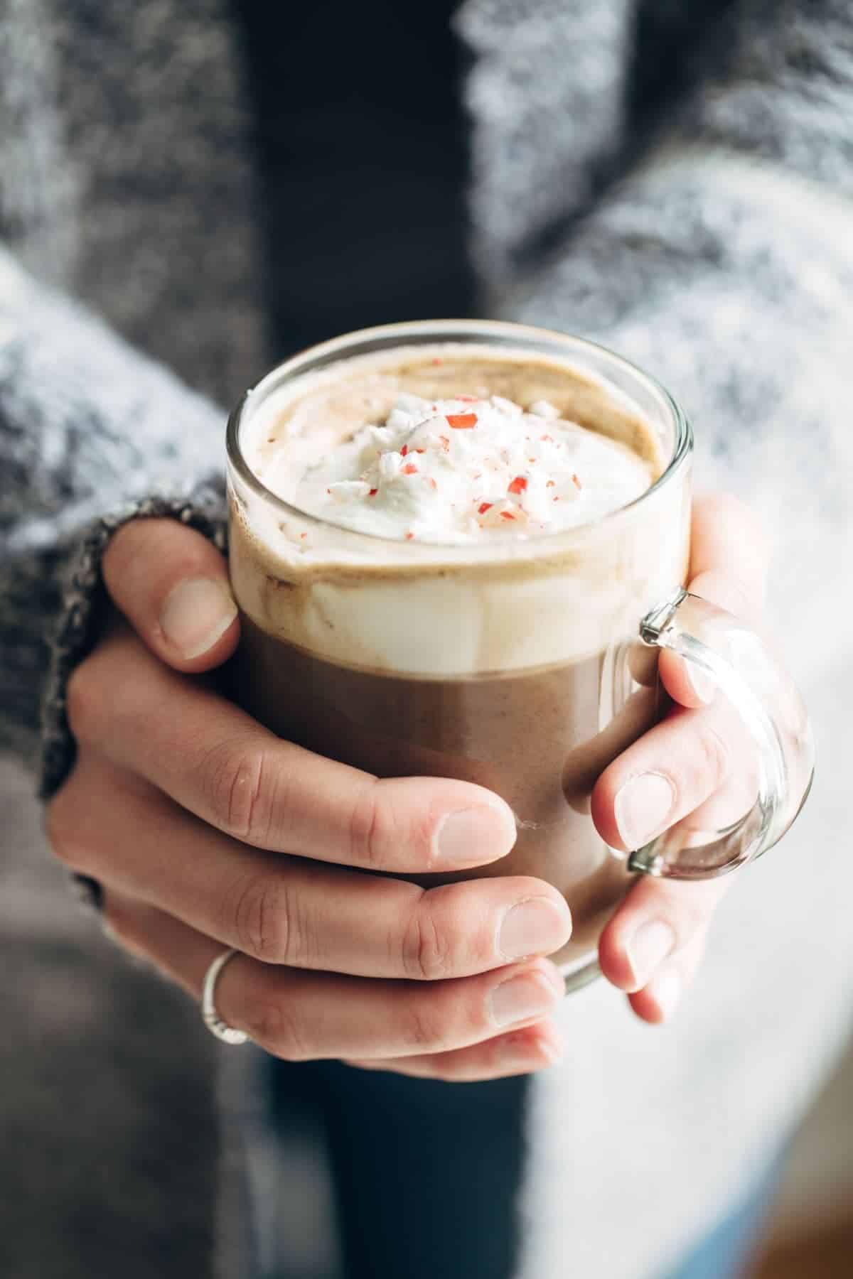 Clear mug of peppermint mocha held in hands. 