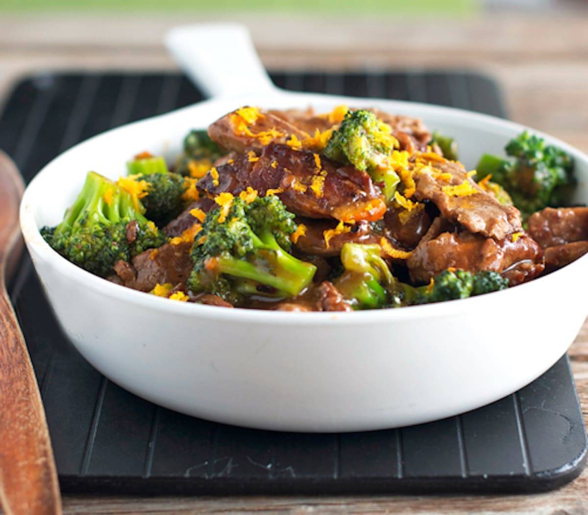 Light orange beef and broccoli in a bowl with orange zest.