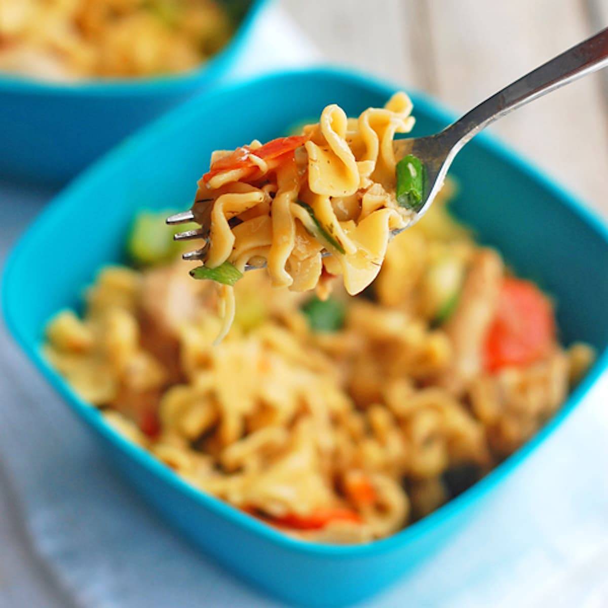 Chicken soup noodles on a fork over a blue bowl.